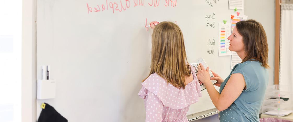 Karen Cooling with a young student writing on the classroom white board