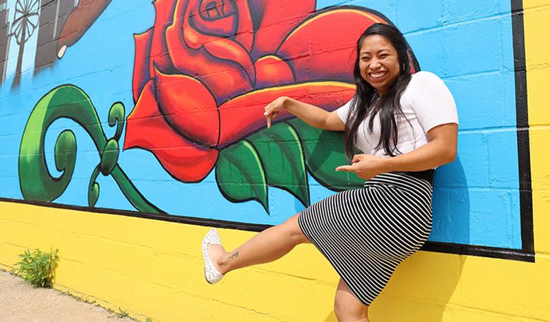 阿尔玛站在锡达拉皮兹市的一幅壁画前，微笑着指着她脚踝上类似的纹身