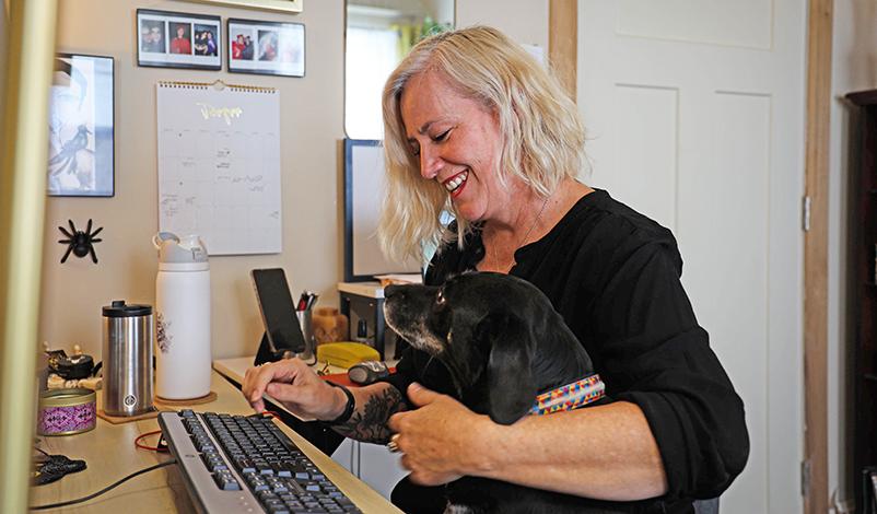 Jennifer working from home, hugging her dog with one arm and typing with the other
